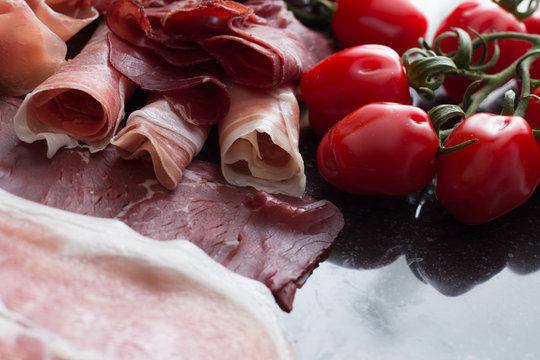 Ham mix. jambon. Traditional Italian and Spanish salting, smoking, dry-cured dish - jamon Serrano and prosciutto crudo sliced with herbs and tomatos on dark stone background. Copy space. Closeup. 