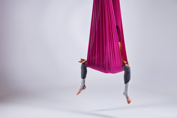 Young woman practices different inversion aerial yoga with a hammock in a white studio. Concept of...