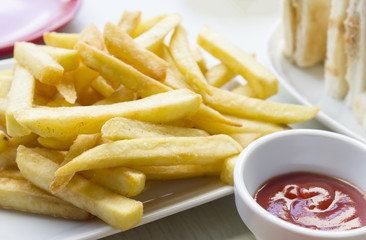 Tasty french fries in dish with tomato sauce on wooden table bac