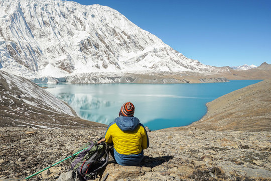 Travel concept: Trekker with tourist sticks and backpack on Tilicho lake. Its 4900m above sea level. Snowly peaks of mountains and Tilicho lake on background.