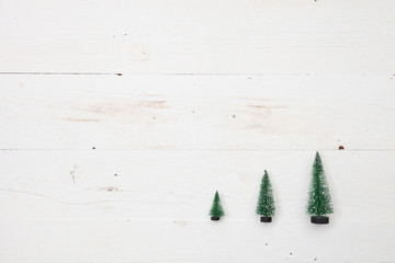 Top view on three little Christmas trees on white wooden background. Holidays and winter concept.