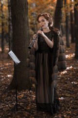 Young woman oboist playing in fall park