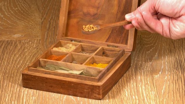 Collection of different oriental indian curry spices in wooden box with fenugreek in wood spoon in senior man hand