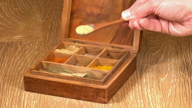 Collection of different oriental indian curry spices in wooden box with ginger in wood spoon in senior man hand