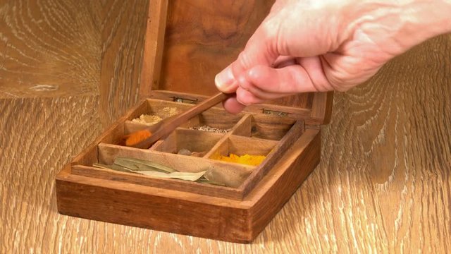 Collection of different oriental indian curry spices in wooden box with paprika in wood spoon in senior man hand