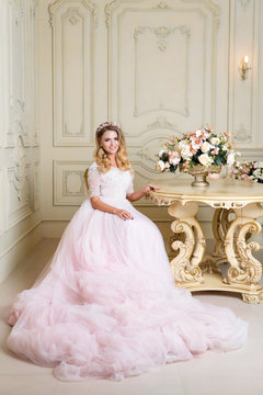 Beautiful blonde woman wearing gorgeous dress and crystal crown posing in luxury classic apartment.