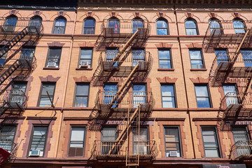 Brown brick building facade in Midtown, New York, with outside fire escapes and windows with room air conditioners