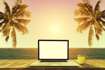 A laptop and a coffee cup on wood table in the sea beach with coconut tree.