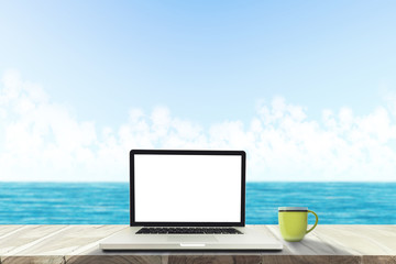 A laptop and a coffee cup on wood table in the sea beach .