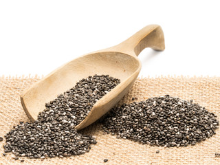 Chia seeds and a wooden spoon on a piece of sack cloth with white background
