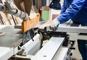 Worker using saw machine to make furniture at carpenters workshop.