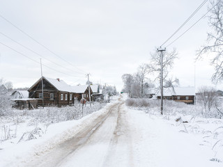 Vanishing snow-covered dirt road with vintage wooden hoses along. Verkhnee Zaozerye village, Novgorodsky region, Russia 
