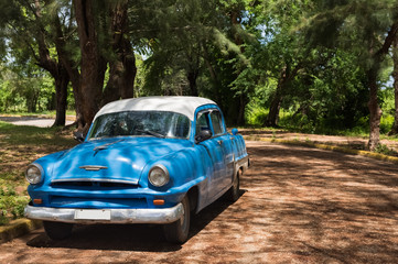 Obraz na płótnie Canvas Amerikanischer blauer Plymouth Oldtimer parkt unter Bäumen in Santa Clara Kuba - Serie Kuba 2016 Reportage