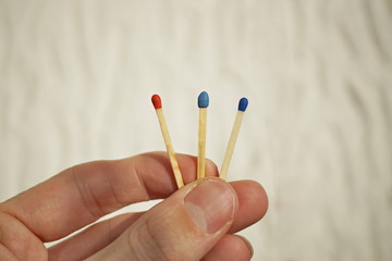 Male hand holding three safety matches, each with a different color of its top as a symbol of challenging choice, option and voting