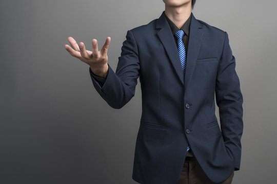 Close up of businessman in blue suit holding something on gray b