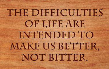 The difficulties of life are intended to make us better, not bitter - quote by unknown author on wooden red oak background