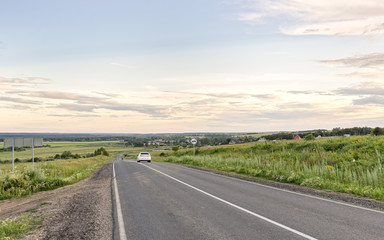 Vanishing straight highway through meadow at sunset in back lit. Silkovo, Kaluzhsky region, Russia.
