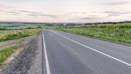 Fototapeta premium Vanishing straight highway through meadow at sunset in back lit. Silkovo, Kaluzhsky region, Russia. 