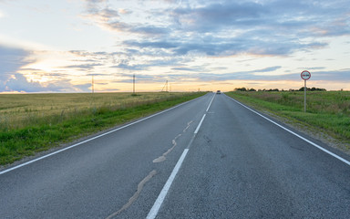 Vanishing straight highway through meadow at sunset in back lit. Silkovo, Kaluzhsky region, Russia.
