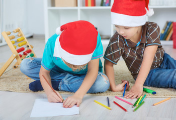Two caucasian boys in Santa red hat painting by the Christmas tree. Christmas concept.