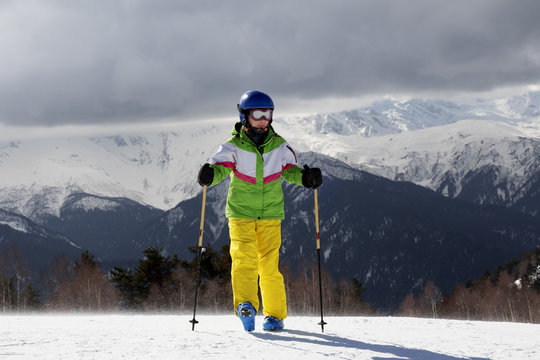 Young skier with ski poles in sun mountains and gray sky before