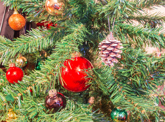 Red ornaments and pine cones on green artificial Christmas tree 