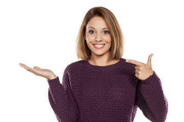 young beautiful woman in a purple sweater and jeans, holding imaginary object on the palm