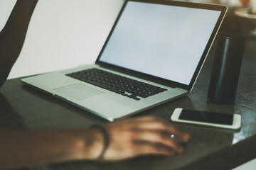 Fototapeta premium View of hands of a man woring with modern laptop standing on concrete table of cafe, mobile phone and portable speaker near laptop, white wall in background