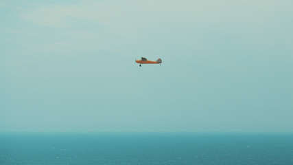Orange one engine prop plane with teal stripes flying above misty ocean in Rio de Janeiro, Brazil, bright sunny day with clear sky
