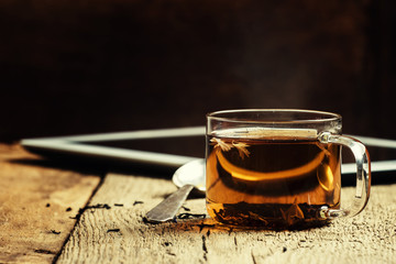 Cup of hot tea and tablet on old wooden table, selective focus