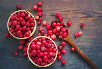Fresh red forest cranberry in a round bowls with a wooden spoon on a wooden table surface. Autumn harvest of wild berries
