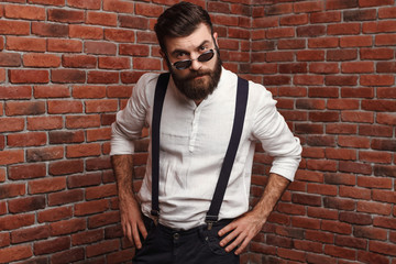 Young handsome man in sunglasses posing over brick background.