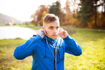 Young runner with earphones outside in sunny autumn nature