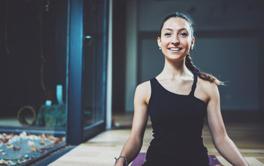 Portrait of gorgeous young woman practicing yoga indoor. Beautiful girl practice meditation asana in class.Calmness and relax, female happiness.Horizontal front view, blurred background.