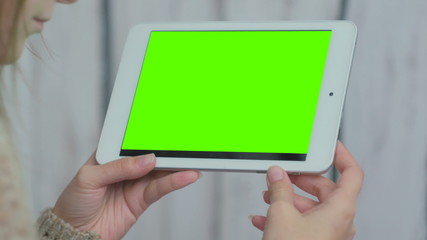 Woman looking at horizontal tablet computer with green screen. Close up shot of woman's hands with pad. White wooden background