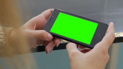 Woman looking at horizontal smartphone with green screen. Close up shot of woman's hands with mobile