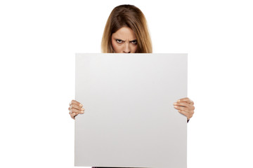 young angry woman  peeking behind blank board for advertising