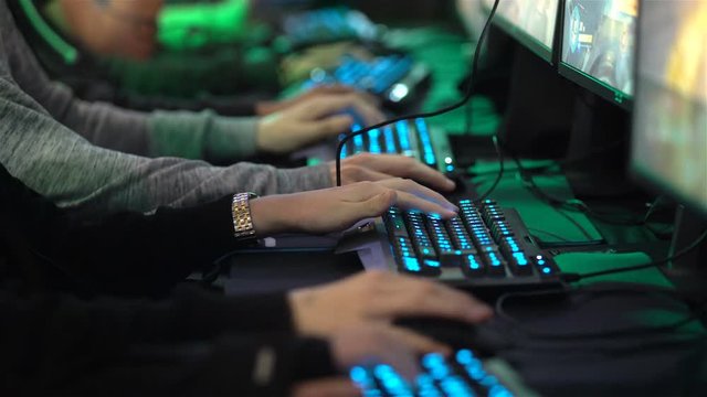 A lot of teenagers playing on computer games. Close-up of hands with keyboards and mouses.