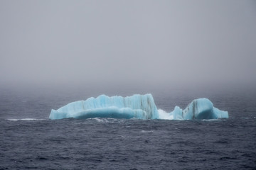 Small blue iceberg drifting on foggy Arctic Ocean