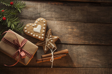 Wrapped in craft paper and ribbon christmas gift with gingerbread cookies, christmas tree twig and cinnamon sticks on a wooden table.