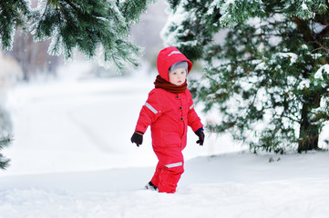 Cute little boy in red winter clothes having fun with snow