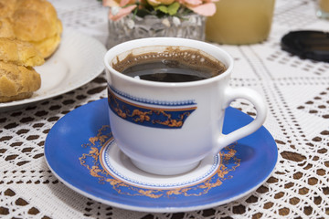 Coffee in the cup with cream puffs on a plate
