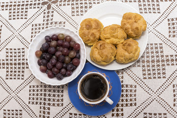 Coffee in the cup with cream puffs on a plate and grapes in a bowl
