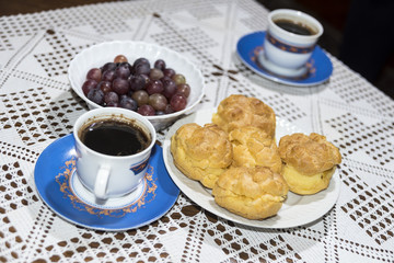 Coffee in the cup with cream puffs on a plate and grapes in a bowl