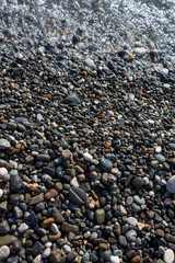 Wet bright shining different colored pebble stones and sea wave