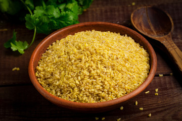 Raw bulgur, wheat grains in bowl on wooden table. Close up view