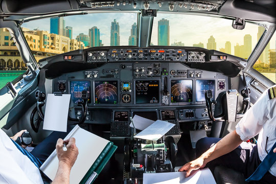 Airplane cockpit flying on Dubai skyscrapers skyline, United Arab Emirates, with pilots arms and blank white papers for copy space.