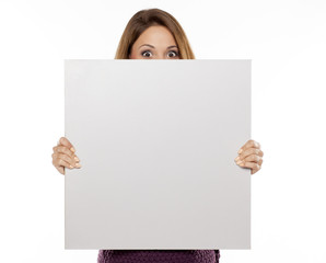 young beautiful woman peeking behind blank board for advertising