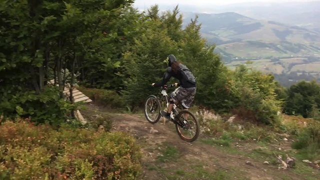 Downhill cyclist rides along a mountain trail and calls in on a trampoline