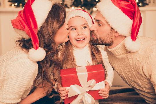 Happy parents kissing daughter and giving xmas present  on bed